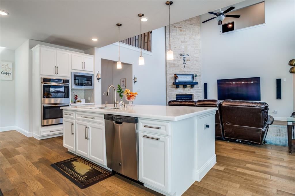 16380 Radstock Road Frisco, TX 75033 - Photo 38 of 39 Kitchen featuring a stone fireplace, white cabinetry, open floor plan, stainless steel appliances, and light wood-style flooring