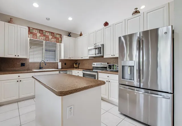 a kitchen with stainless steel appliances granite countertop a refrigerator a sink a stove a kitchen island and a window