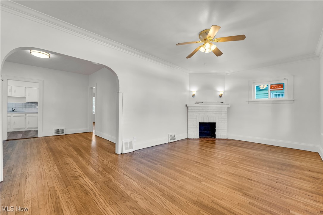 3320 Berea Road Cleveland, OH 44111 - Photo 6 of 26 Unfurnished living room featuring a fireplace, arched walkways, crown molding, light wood-style flooring, and a ceiling fan