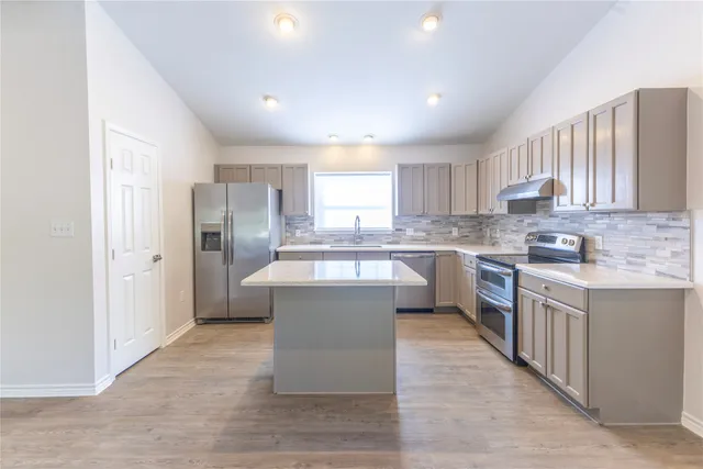 a kitchen with stainless steel appliances granite countertop a refrigerator a sink dishwasher a stove and white countertops with wooden floor