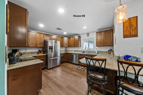 a kitchen with stainless steel appliances kitchen island granite countertop a refrigerator a stove a sink a dining table and chairs with wooden floor