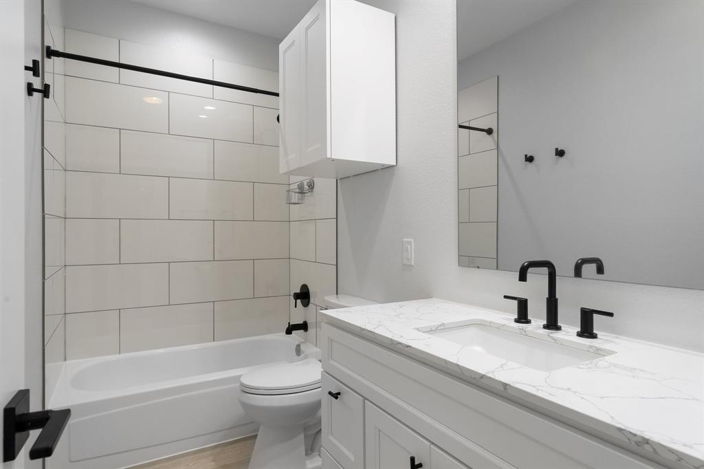 14140 Regency Place Dallas, TX 75254 - Photo 29 of 38 Bathroom featuring a white subway tile tub surround, black plumbing fixtures, a white vanity with a rectangular undermount sink, a stone-finish countertop, and a wall-mounted medicine cabinet