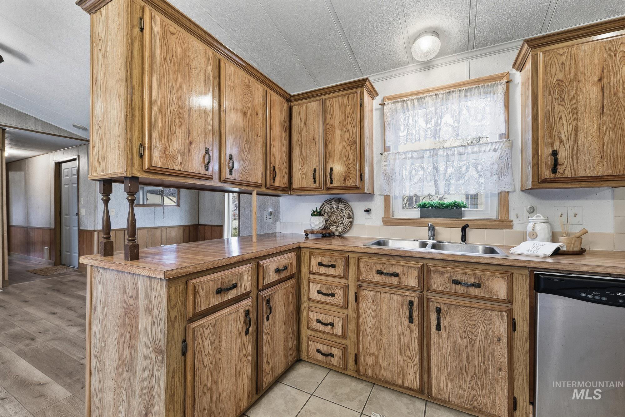 5200 Midway, Unit TRIR 20 Caldwell, ID 83607 - Photo 14 of 31 Kitchen featuring dishwasher, a peninsula, brown cabinets, light tile patterned floors, and wood walls
