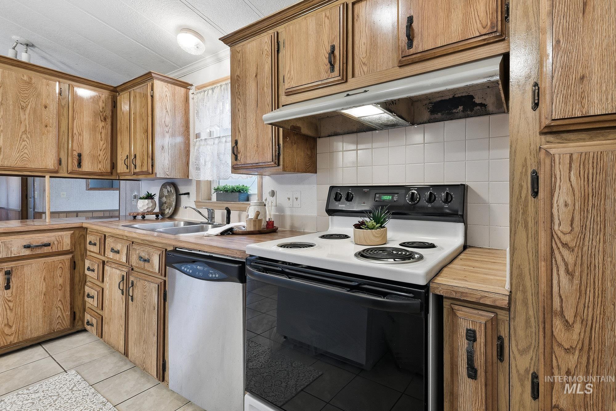 5200 Midway, Unit TRIR 20 Caldwell, ID 83607 - Photo 15 of 31 Kitchen with electric range, under cabinet range hood, light countertops, stainless steel dishwasher, and brown cabinets