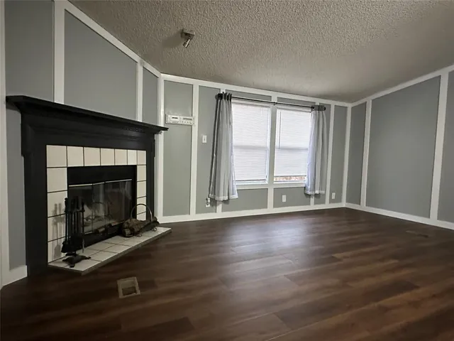 a view of an empty room with wooden floor fireplace and a window