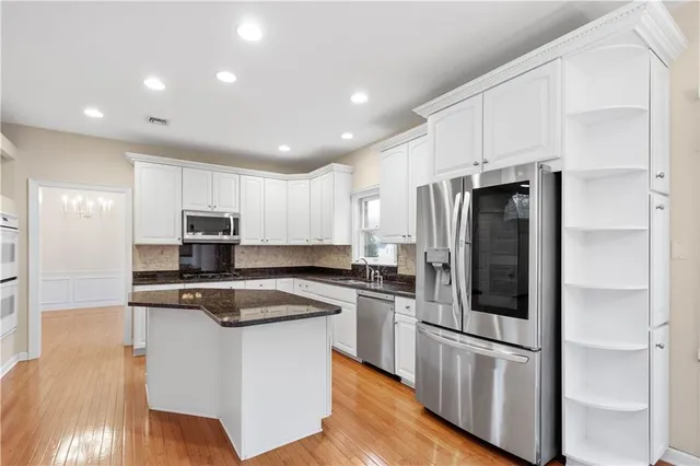 a kitchen with stainless steel appliances granite countertop a refrigerator a stove a sink and white cabinets with wooden floor