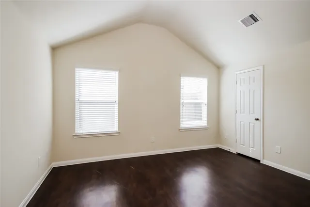 an empty room with wooden floor closet and windows