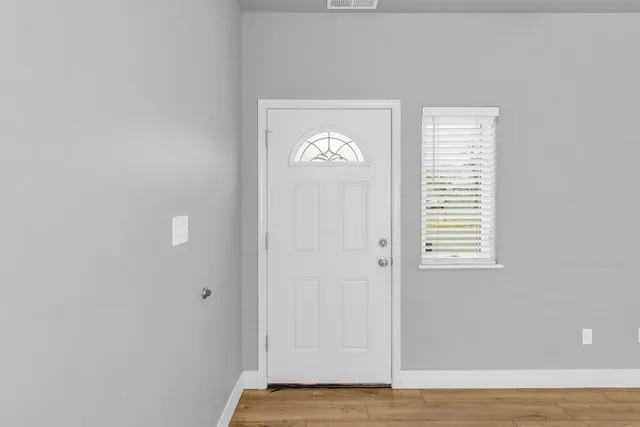 a view of an empty room with wooden floor and a window