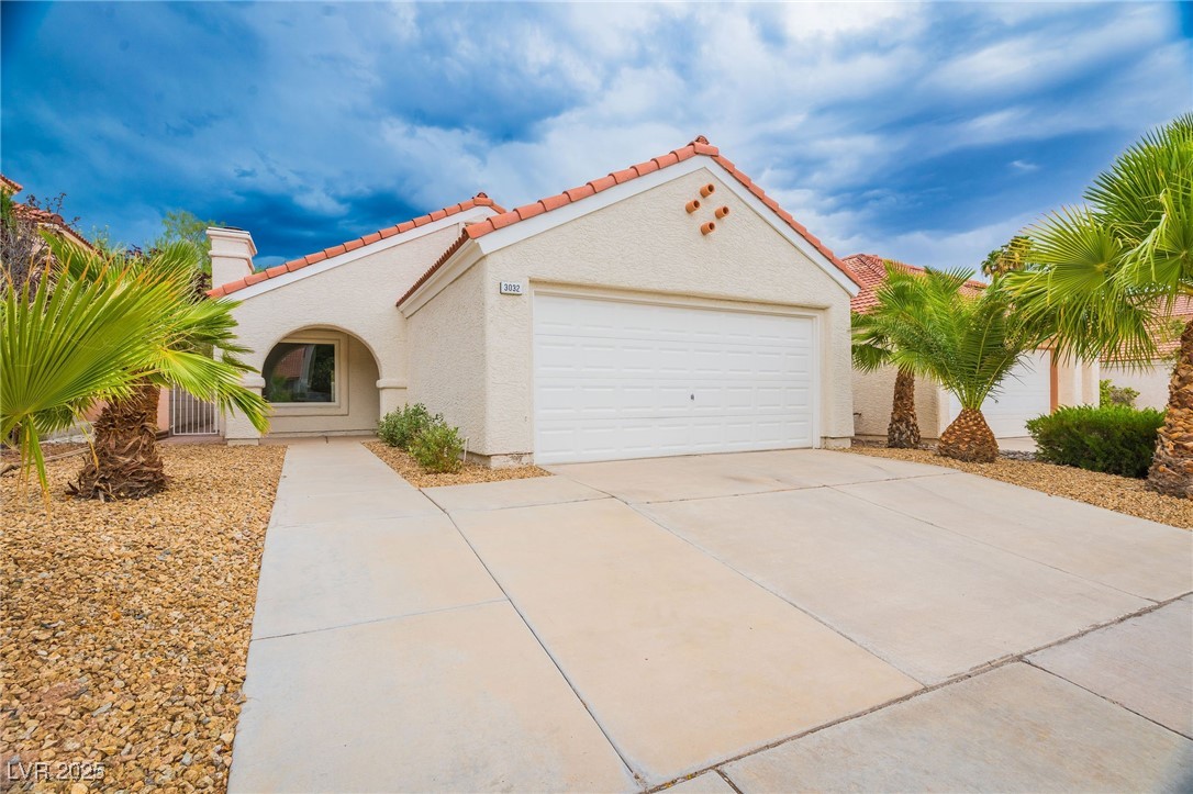 Mediterranean / spanish-style home featuring stucco siding, a tiled roof, concrete driveway, a chimney, and a garage