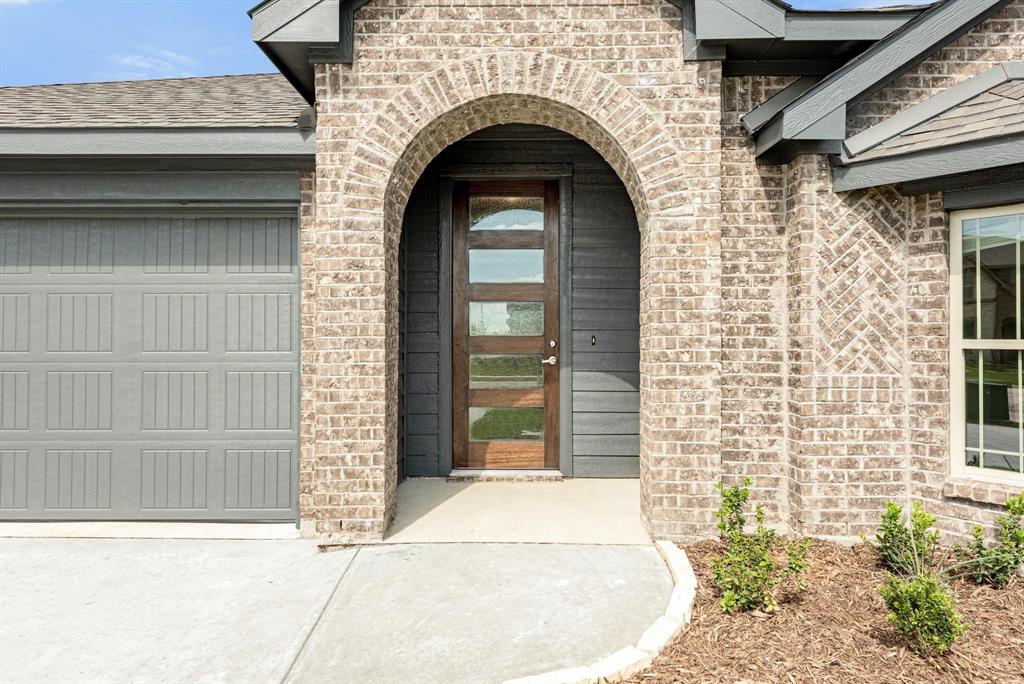920 Elk Ridge Run Godley, TX 76044 - Photo 3 of 34 Brick exterior featuring an arched entryway, modern wood-finish front door with privacy glass, and a paneled garage door