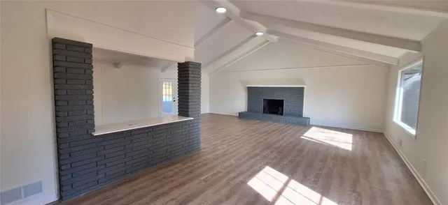 an empty room with wooden floor fireplace and windows