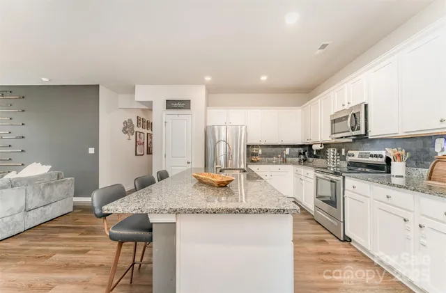 a kitchen with stainless steel appliances granite countertop a sink a stove a refrigerator cabinets and living room view