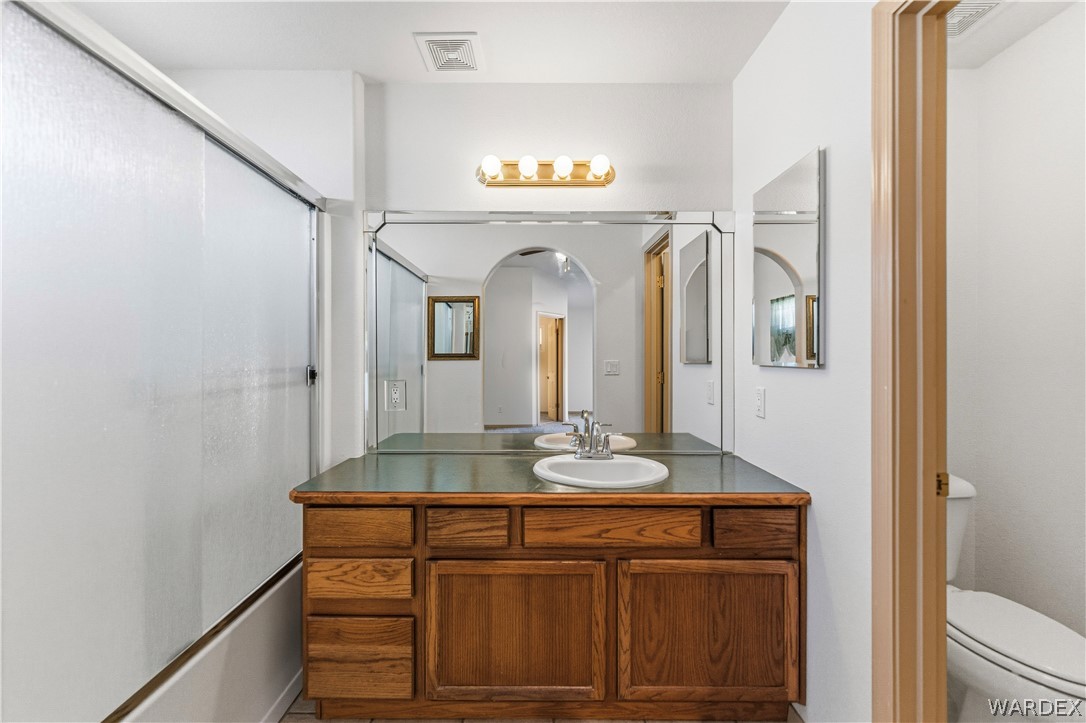 3973 Prairie View Drive Kingman, AZ 86409 - Photo 20 of 34 Bathroom featuring a wooden vanity with a single sink, a large mirror, and a shower with frosted glass doors