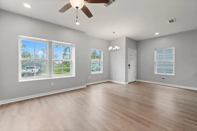 an empty room with wooden floor chandelier and windows
