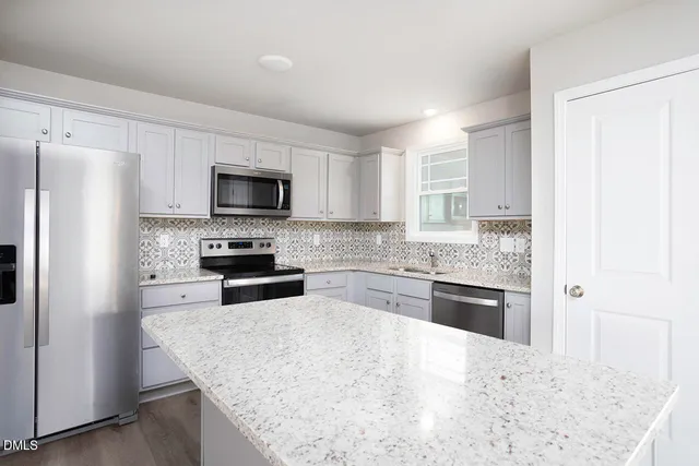 a kitchen with granite countertop white cabinets stainless steel appliances and a window