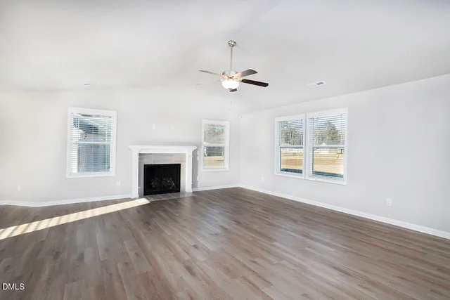 an empty room with wooden floor fireplace and windows
