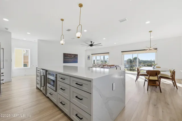 a large white kitchen with stainless steel appliances granite countertop a stove oven a sink dishwasher and a dining table with the living room view