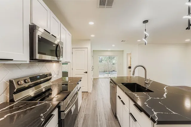 a kitchen with stainless steel appliances granite countertop a refrigerator a sink dishwasher a stove and a refrigerator with wooden floor