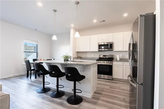 a kitchen with stainless steel appliances granite countertop a refrigerator a stove a sink a dining table and chairs with wooden floor