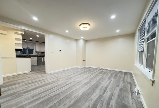 an empty room with wooden floor and a kitchen