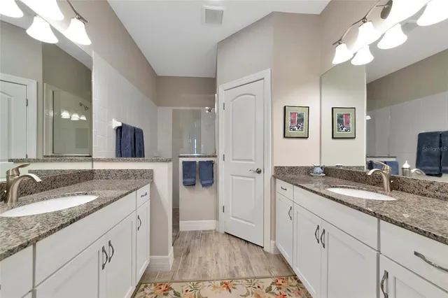 a spacious bathroom with a granite countertop double vanity sink a mirror and shower