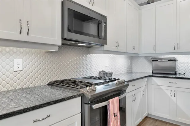 a kitchen with stainless steel appliances granite countertop white cabinets and a stove a oven with white countertops