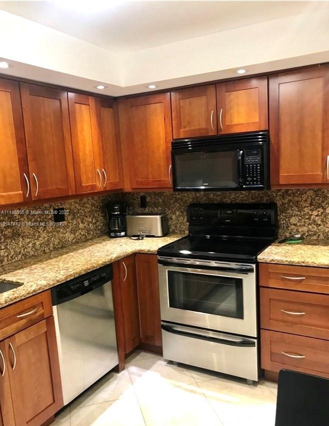 9511 Collins Avenue, Unit 308 Surfside, FL 33154 - Photo 11 of 14 a kitchen with stainless steel appliances wooden cabinets and a stove top oven