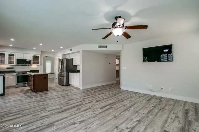 a view of a livingroom with a kitchen island wooden floor and a ceiling fan