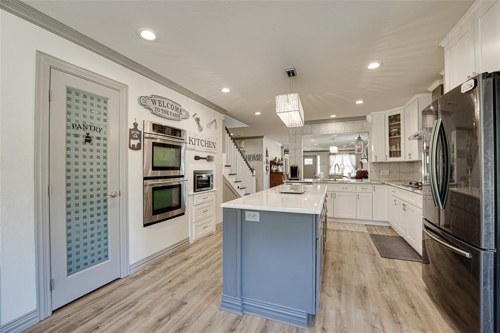 521 Bakers Branch Road Waxahachie, TX 75167 - Photo 17 of 37 Kitchen featuring an expansive center island with a light countertop, white cabinetry, stainless steel double wall ovens, and wood-finish flooring