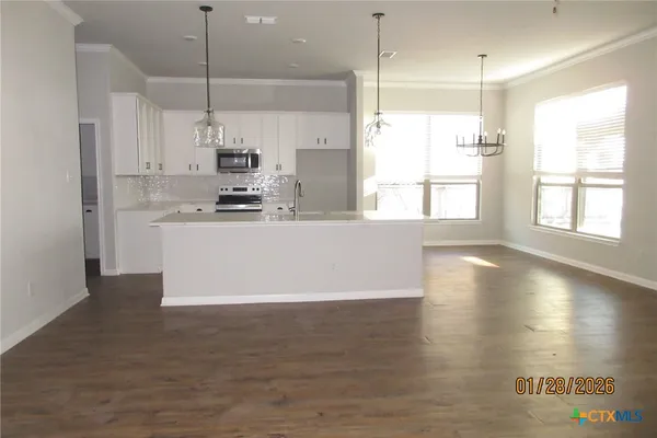 a view of an empty room with kitchen and a window