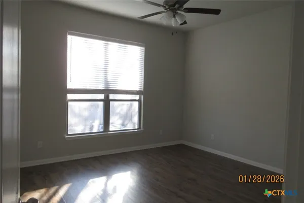 a view of an empty room with wooden floor and a ceiling fan