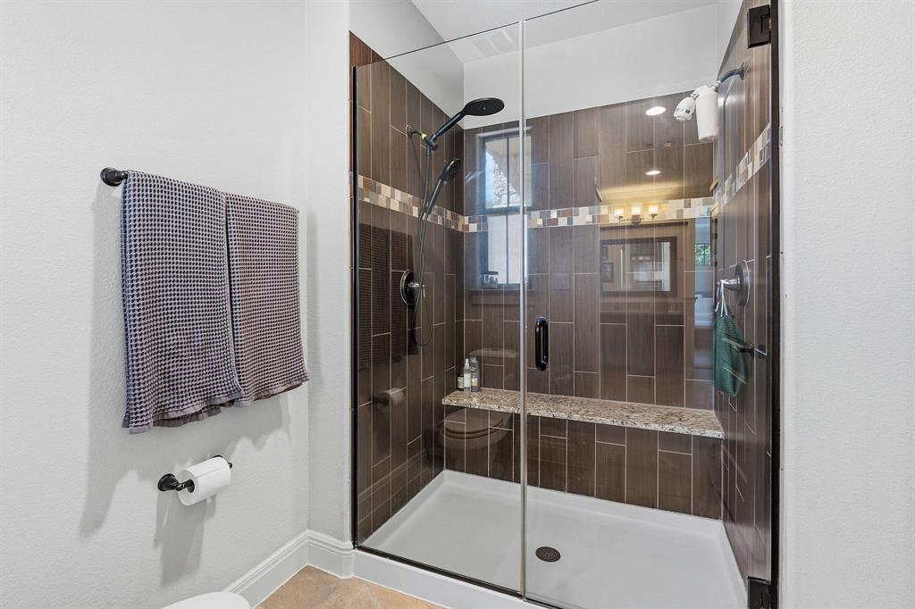 15317 Falconhead Grove Loop Austin, TX 78738 - Photo 17 of 29 A glass-enclosed shower boasts a built-in bench and a modern tiled interior.