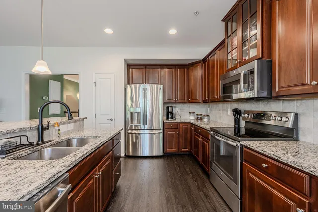 a kitchen with stainless steel appliances granite countertop wooden cabinets a sink dishwasher a stove and a refrigerator with wooden floor