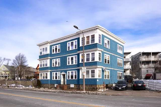 a front view of a building with lot of cars and trees