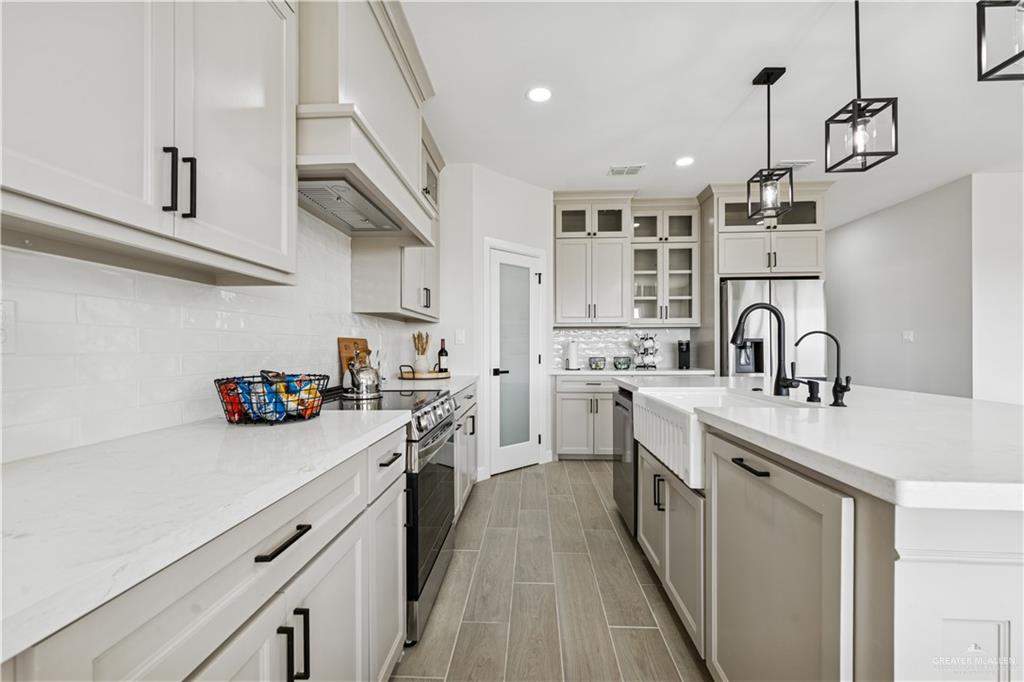 1013 Azalea Street Mission, TX 78573 - Photo 13 of 35 Kitchen featuring glass insert cabinets, a kitchen island with sink, recessed lighting, light stone counters, and decorative light fixtures