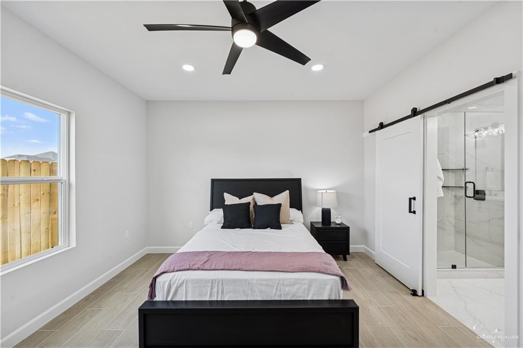 1013 Azalea Street Mission, TX 78573 - Photo 19 of 35 Bedroom with a barn door, wood tiled floors, recessed lighting, ceiling fan, and ensuite bath