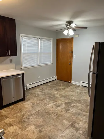 an empty room with chandelier fan and kitchen view
