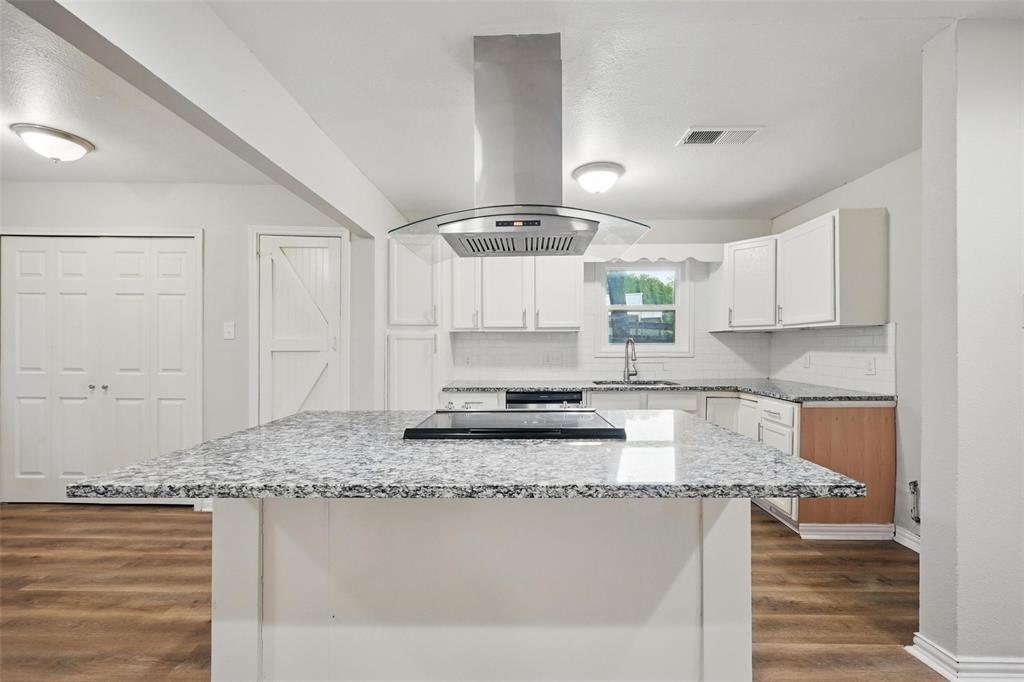 1003 Pecan Avenue Greenville, TX 75401 - Photo 6 of 25 a kitchen with kitchen island granite countertop a sink cabinets and wooden floor