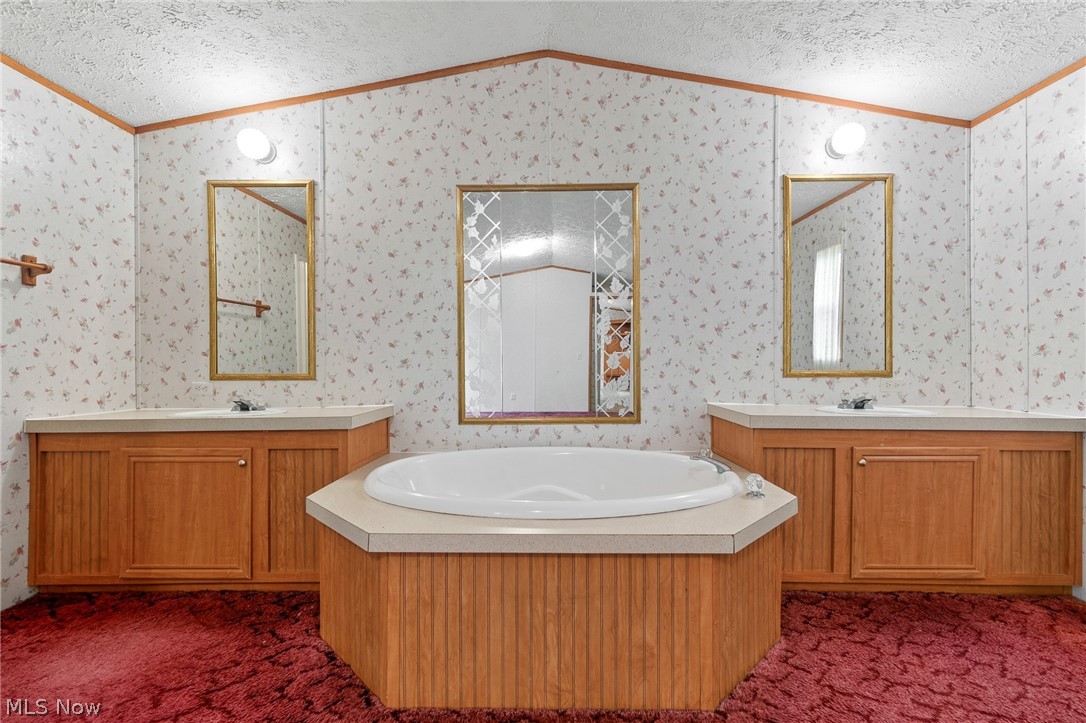 8472 Azalea Road Southwest Dennison, OH 44621 - Photo 27 of 35 Luxurious primary bathroom suite featuring a sunken octagonal soaking tub with wood-finish cabinetry surround, dual vanities with wood-finish cabinetry and framed mirrors, polished fixtures, recessed lighting, and decorative tile walls throughout
