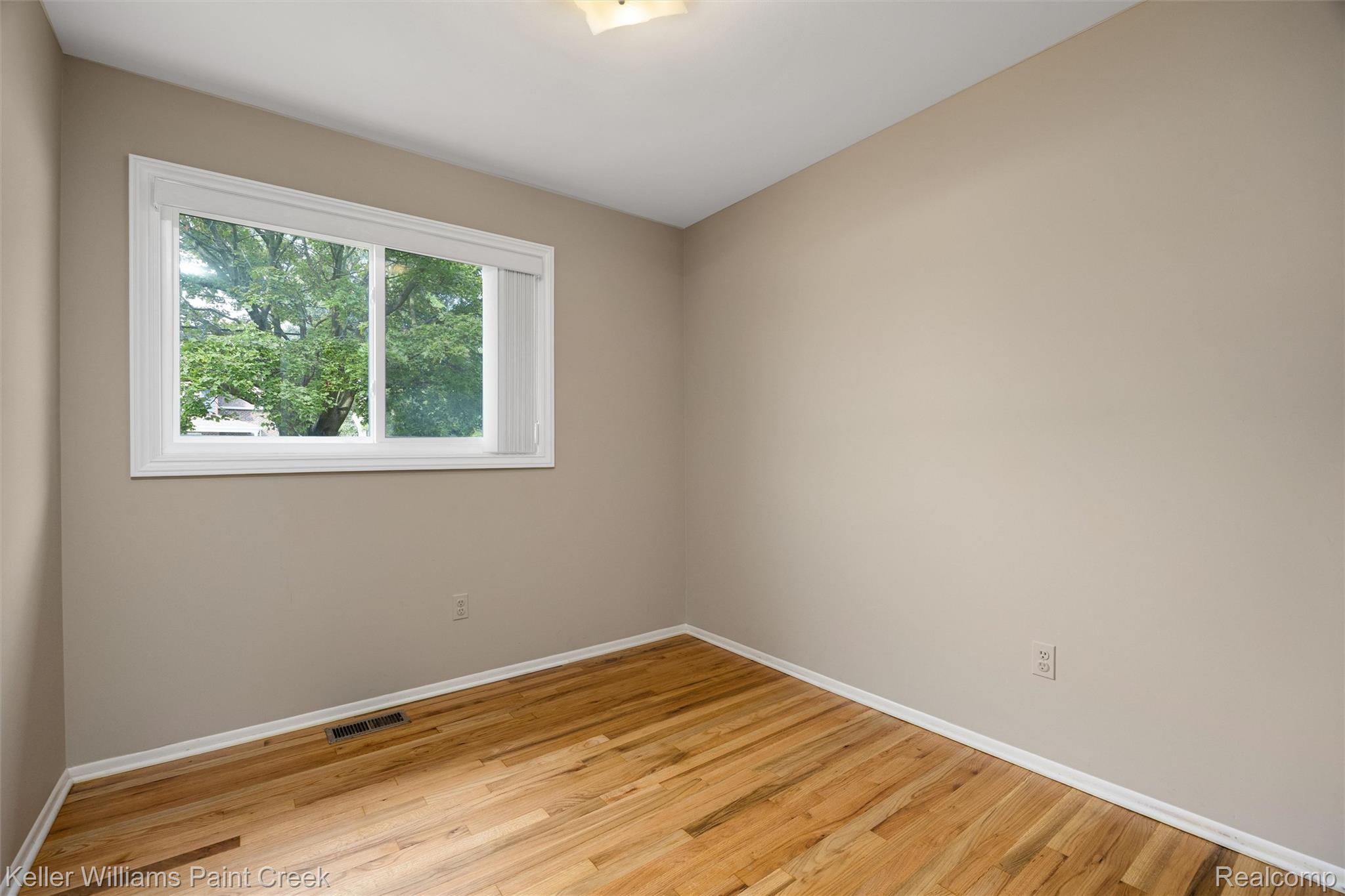 1766 Henry Ruff Road Garden City, MI 48135 - Photo 15 of 36 Bright, light-filled bedroom showcasing rich wood-finish hardwood flooring, neutral taupe walls, and a large casement window with white trim framing natural outdoor scenery