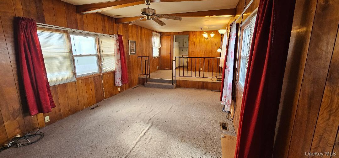 1964 River Road, Unit 35 Calverton, NY 11933 - Photo 3 of 16 Carpeted empty room with wooden walls, beam ceiling, and ceiling fan