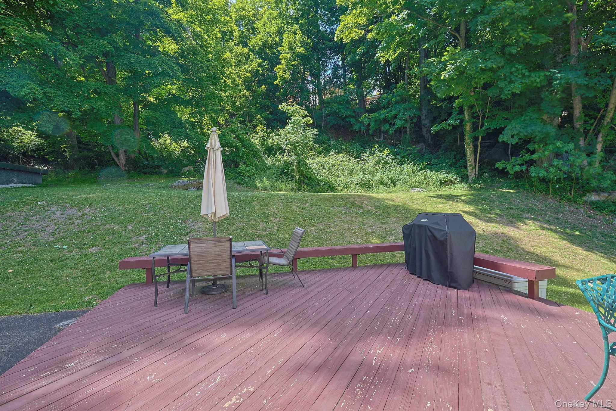 9 Library Road Tuxedo Park, NY 10987 - Photo 34 of 37 Expansive wood-finish deck with integrated bench seating, overlooking a sloped grassy area and mature trees