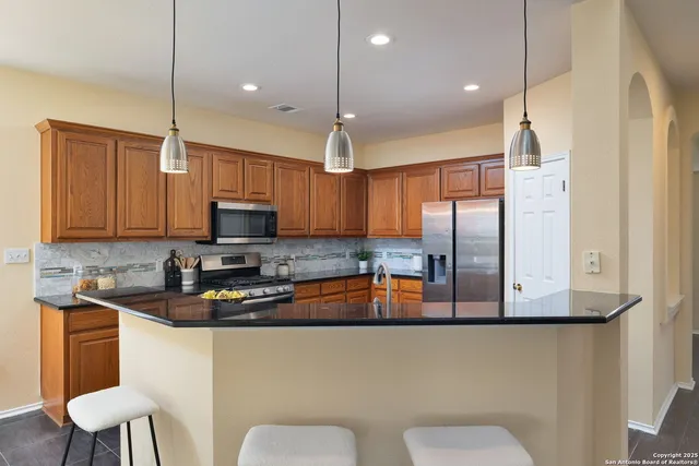 a kitchen with stainless steel appliances granite countertop a sink a stove a refrigerator a kitchen island with wooden cabinets and floor