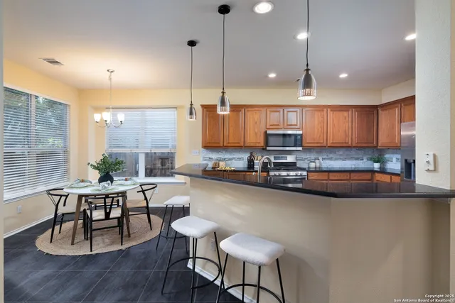 a kitchen with stainless steel appliances granite countertop a stove top oven a sink dishwasher a dining table and chairs with wooden floor