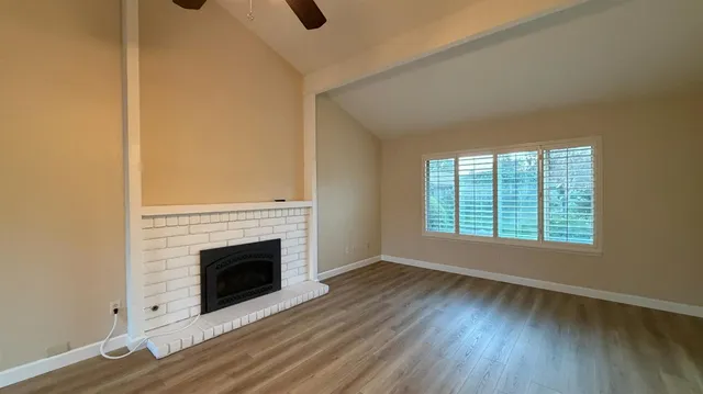 an empty room with wooden floor fireplace and windows