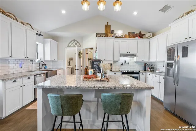 a kitchen with stainless steel appliances granite countertop a sink a stove a refrigerator cabinets and chairs