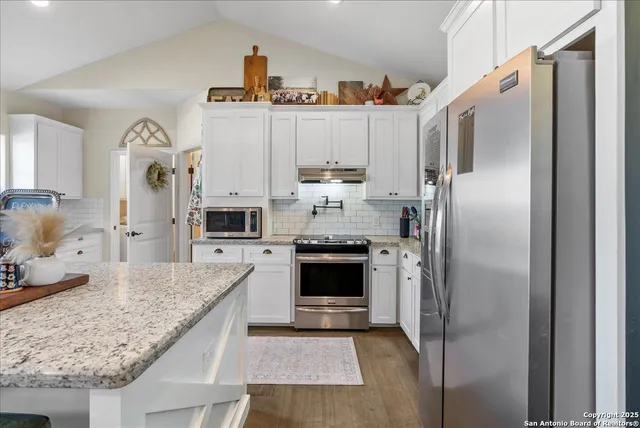 a kitchen with stainless steel appliances granite countertop a refrigerator a oven and white cabinets with wooden floor