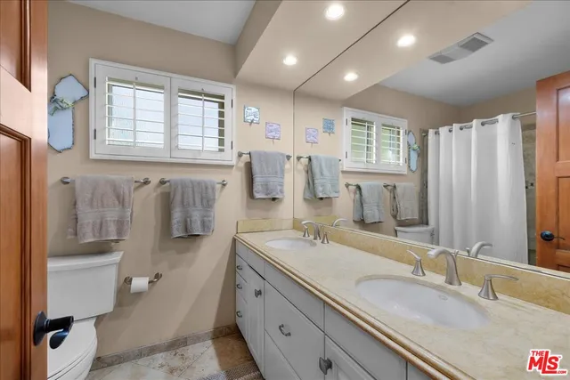 a spacious bathroom with double vanity a toilet a mirror and a shower
