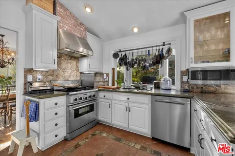 a kitchen with stainless steel appliances granite countertop a stove a sink dishwasher and white cabinets with wooden floor