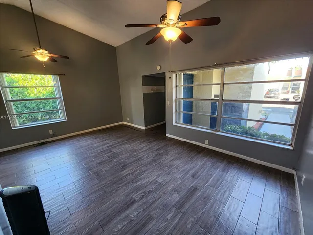 an empty room with wooden floor fan and windows